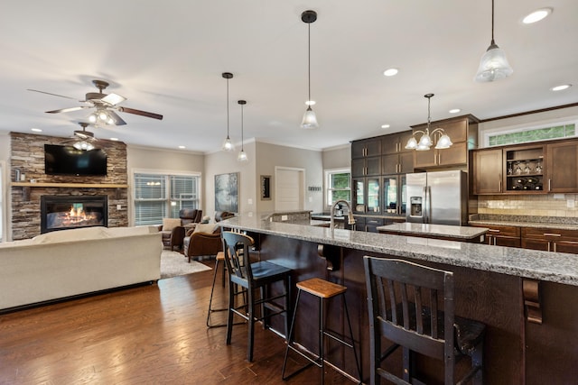 kitchen featuring decorative backsplash, a breakfast bar area, ceiling fan, stainless steel refrigerator with ice dispenser, and light stone counters