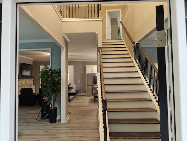 staircase with baseboards, ornamental molding, wood finished floors, and a stone fireplace