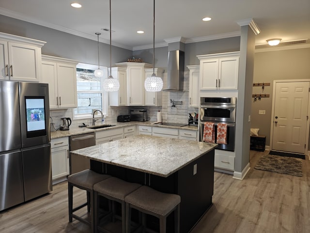 kitchen featuring light wood-type flooring, wall chimney exhaust hood, white cabinetry, a sink, and appliances with stainless steel finishes