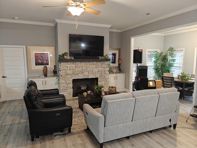 living room featuring crown molding, ceiling fan, a stone fireplace, and light wood-type flooring
