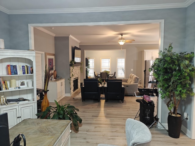 interior space featuring ornamental molding, a stone fireplace, light wood-style floors, baseboards, and a ceiling fan