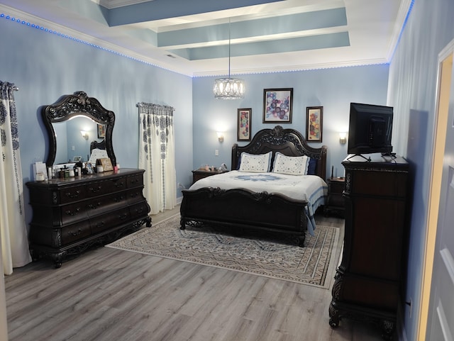 bedroom featuring an inviting chandelier, a raised ceiling, crown molding, and wood finished floors