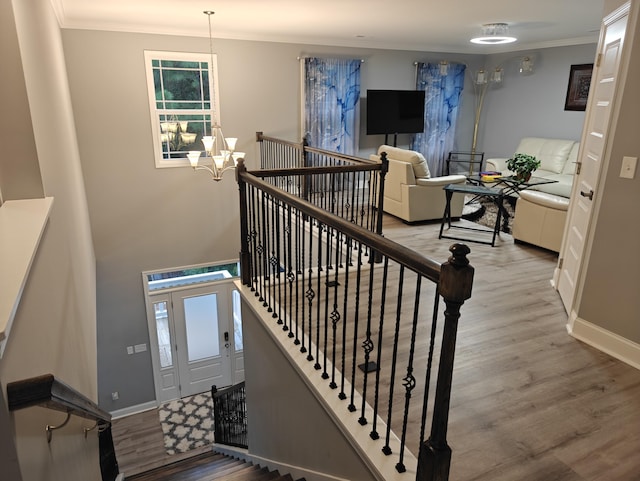 stairway with baseboards, a notable chandelier, ornamental molding, and wood finished floors