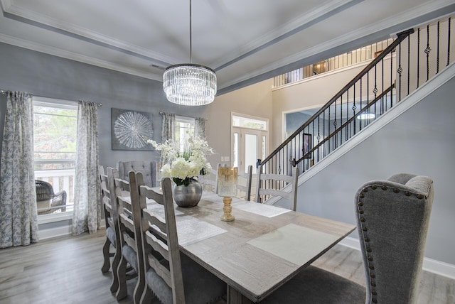 dining area with ornamental molding, wood finished floors, stairway, a raised ceiling, and a chandelier