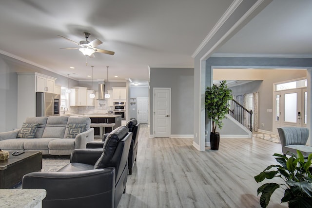 living area with stairway, ceiling fan, light wood finished floors, and crown molding