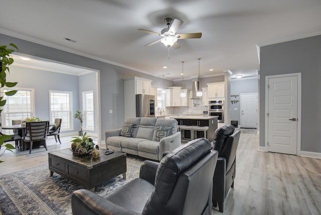 living area featuring a ceiling fan, visible vents, crown molding, baseboards, and light wood finished floors