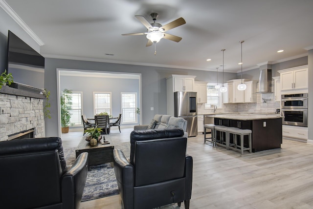 living area featuring light wood finished floors, ceiling fan, a fireplace, and ornamental molding