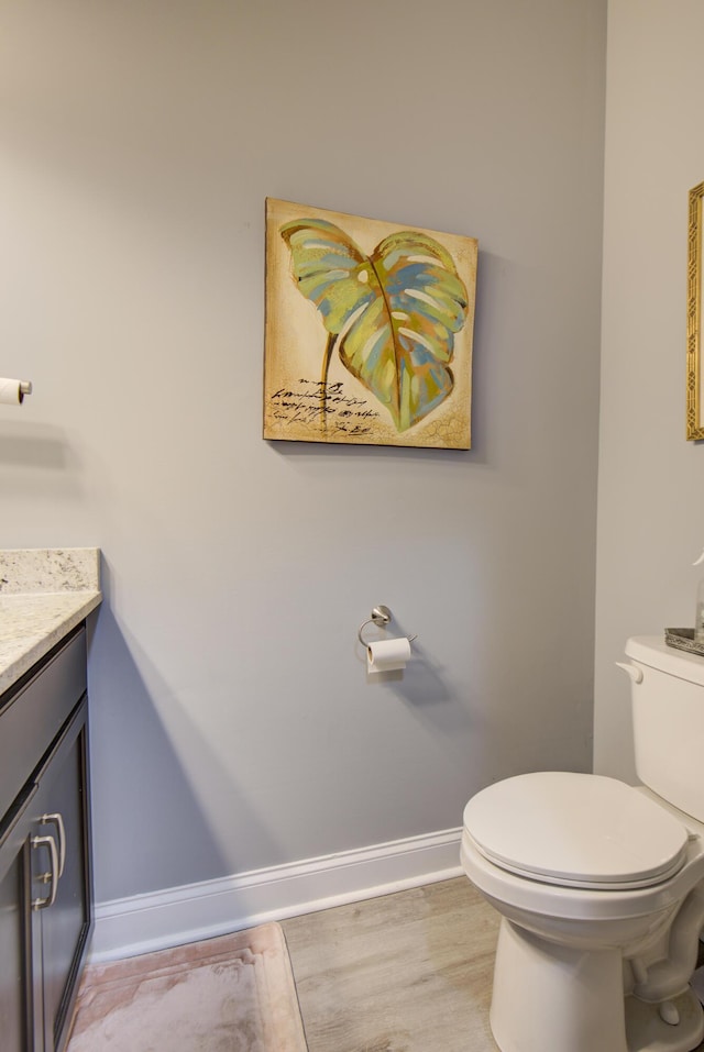 half bathroom featuring baseboards, wood finished floors, toilet, and vanity