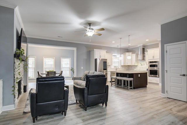 living area featuring a ceiling fan, baseboards, ornamental molding, and light wood-type flooring
