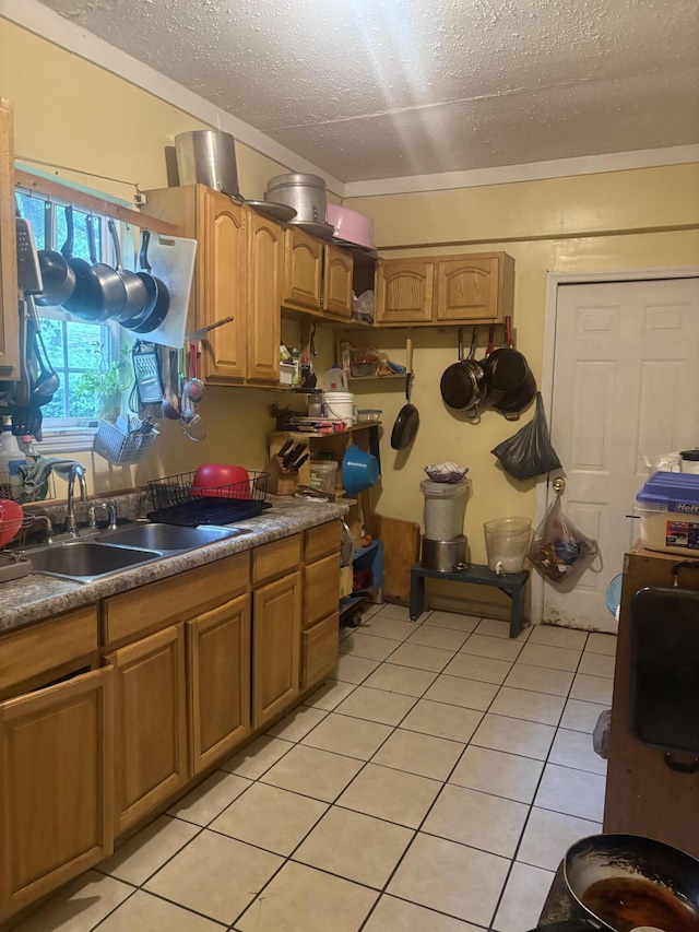 kitchen with a textured ceiling, brown cabinets, light tile patterned flooring, and a sink