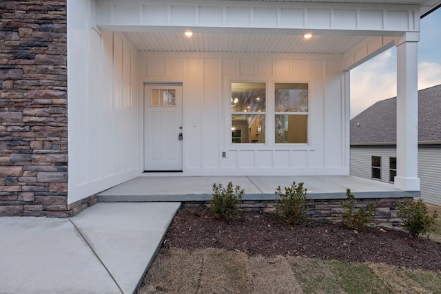 doorway to property with covered porch, board and batten siding, and stone siding