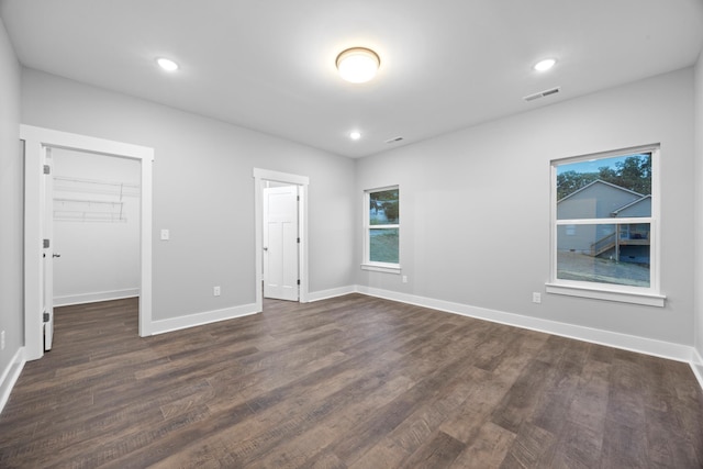 unfurnished bedroom with a walk in closet, baseboards, dark wood-style flooring, and visible vents