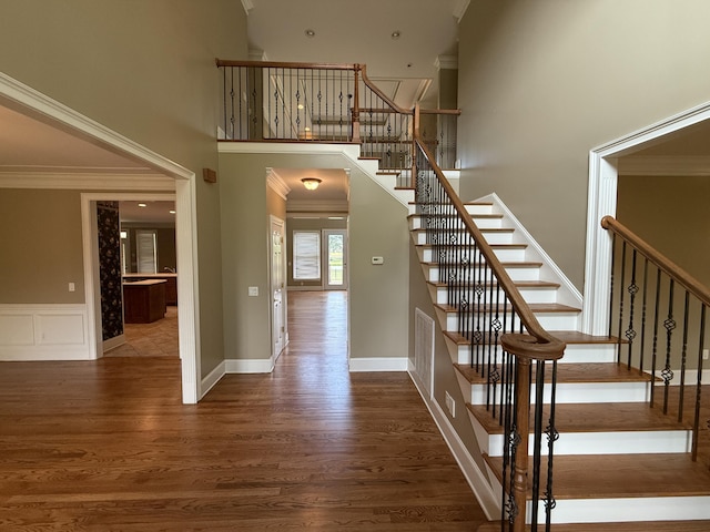 stairway with baseboards, ornamental molding, a high ceiling, and wood finished floors