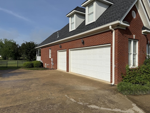 view of home's exterior with brick siding, fence, a garage, a shingled roof, and concrete driveway
