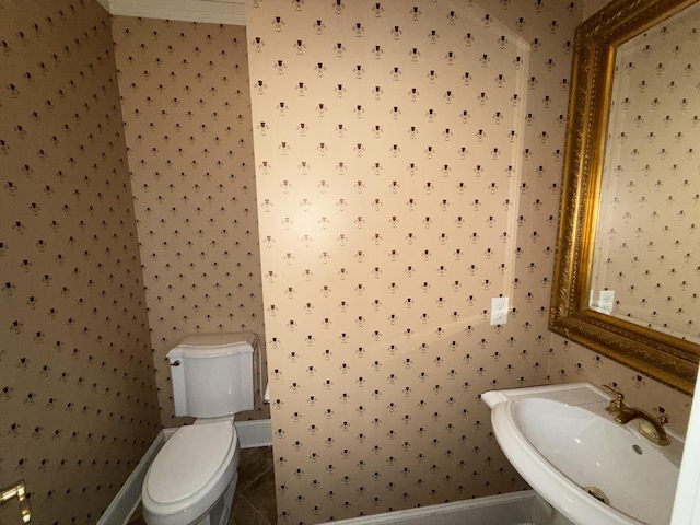 half bath with toilet, baseboards, wallpapered walls, and a sink