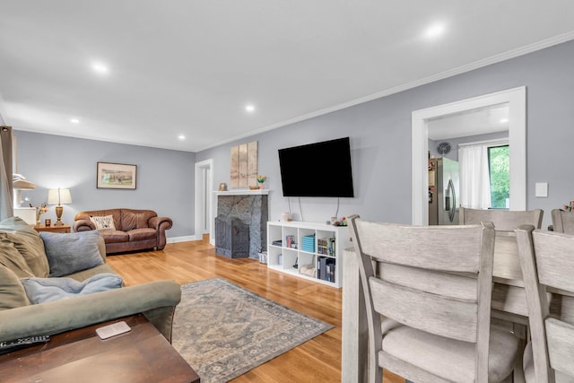 living room with crown molding, recessed lighting, a stone fireplace, and wood finished floors