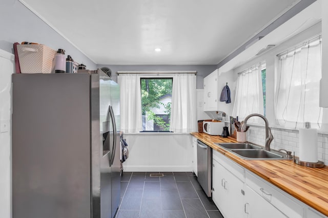 kitchen featuring white cabinetry, a sink, wood counters, backsplash, and stainless steel appliances