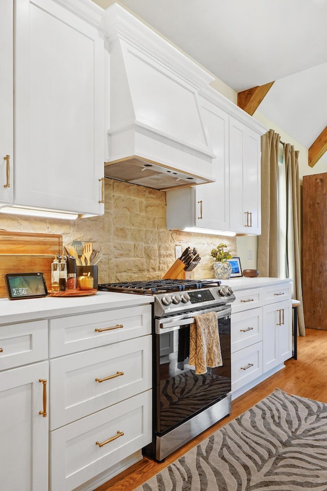 kitchen featuring backsplash, stainless steel range with gas stovetop, light wood-type flooring, premium range hood, and white cabinetry