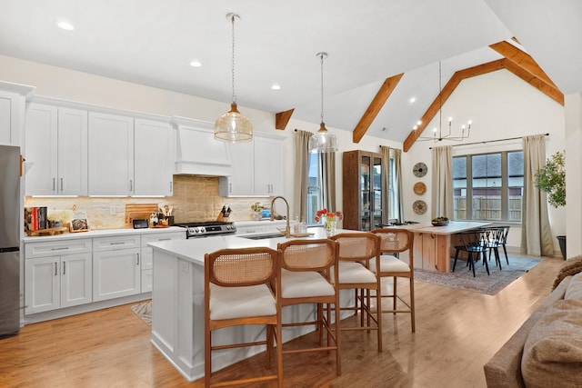 kitchen featuring custom exhaust hood, a center island with sink, tasteful backsplash, a sink, and appliances with stainless steel finishes