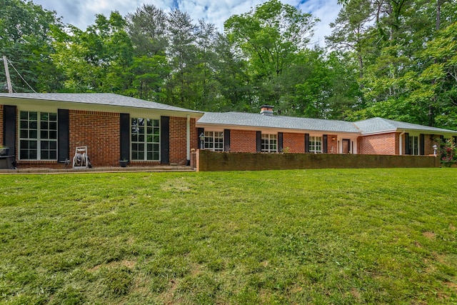 rear view of property with a yard, brick siding, and a chimney