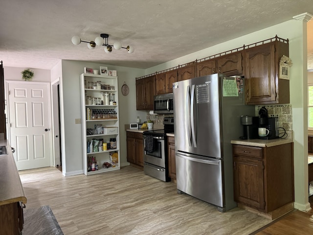 kitchen with stainless steel appliances, a textured ceiling, open shelves, light wood-style flooring, and backsplash
