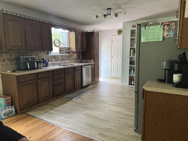 kitchen featuring a sink, stainless steel dishwasher, light countertops, and light wood-style floors