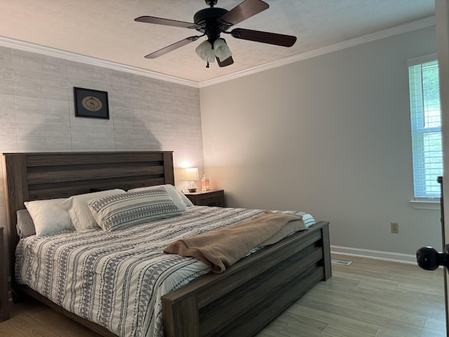 bedroom featuring crown molding, wood finished floors, baseboards, and an accent wall