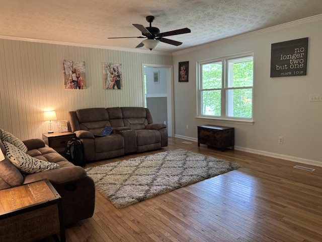 living area featuring a ceiling fan, wood-type flooring, crown molding, visible vents, and baseboards
