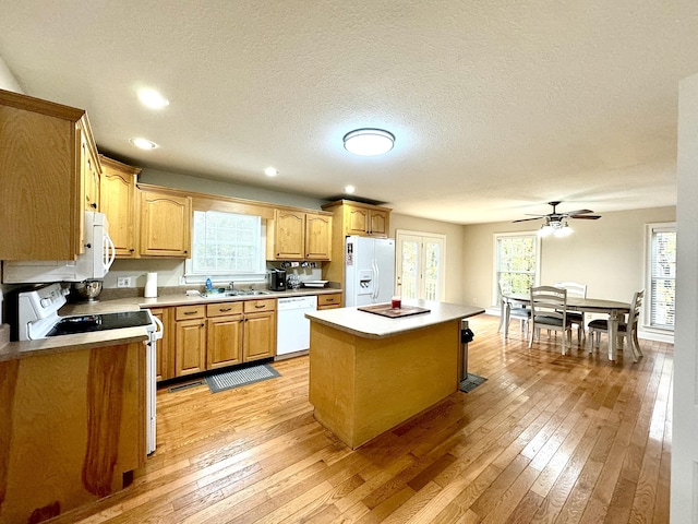 kitchen featuring white appliances, a sink, a center island, and light wood-style floors