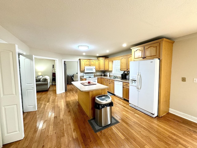 kitchen featuring a sink, light wood-type flooring, white appliances, light countertops, and a kitchen island