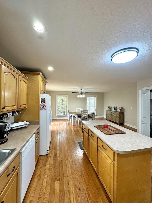 kitchen featuring light wood finished floors, a textured ceiling, white appliances, light countertops, and a kitchen island