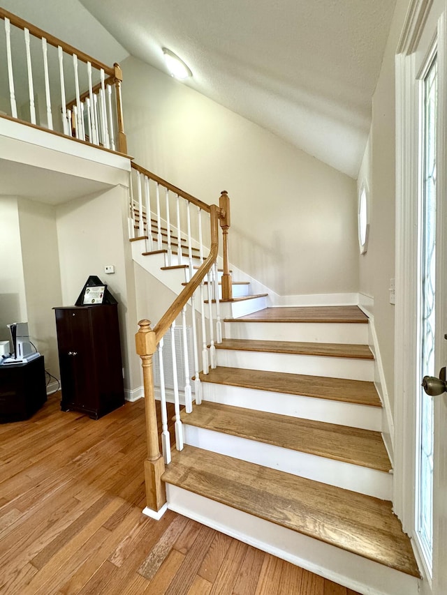 stairs with vaulted ceiling, wood finished floors, and a healthy amount of sunlight
