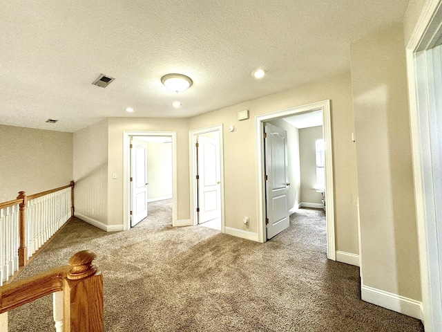 empty room with carpet flooring, a textured ceiling, visible vents, baseboards, and recessed lighting