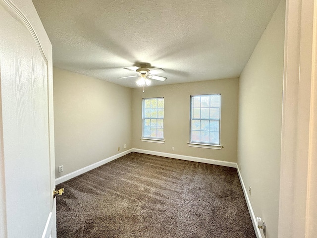 empty room featuring a ceiling fan, baseboards, dark colored carpet, and a textured ceiling