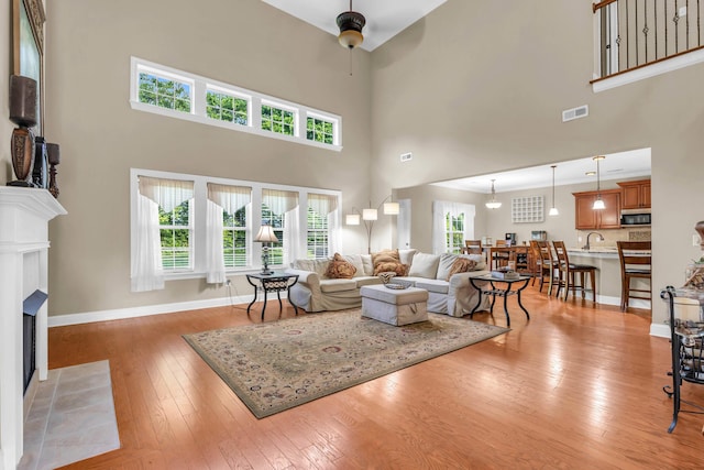 8358 Front Gate Cir, Ooltewah, TN 37363 - living area featuring ceiling fan, a fireplace with flush hearth, light wood-style floors, a towering ceiling, and baseboards