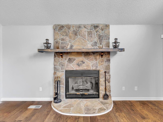 detailed view of a textured ceiling, wood finished floors, baseboards, and a stone fireplace