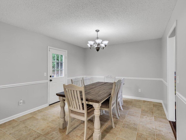 dining room with a chandelier, a textured ceiling, baseboards, and light stone finish floors