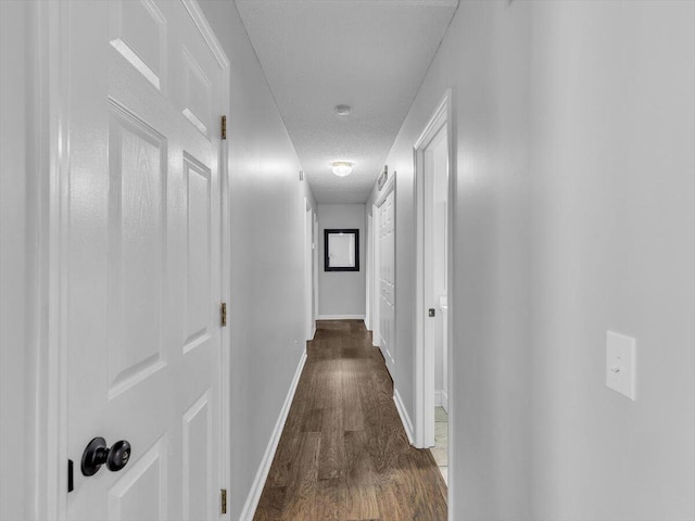 hallway with wood finished floors, baseboards, and a textured ceiling