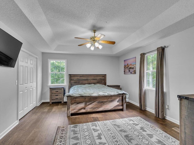 bedroom featuring a tray ceiling, wood finished floors, a textured ceiling, baseboards, and a ceiling fan