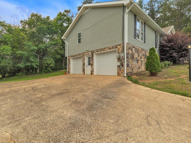 view of side of home with stone siding, an attached garage, and driveway