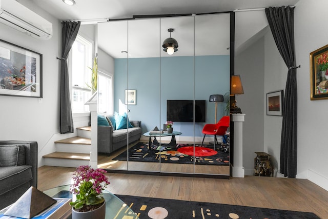 living area featuring an AC wall unit, wood finished floors, and stairs