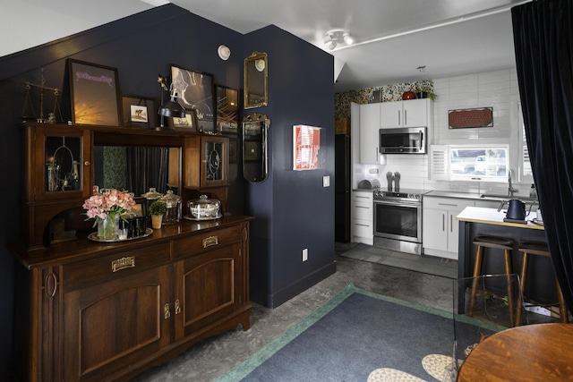 kitchen with appliances with stainless steel finishes, a sink, white cabinetry, and unfinished concrete floors