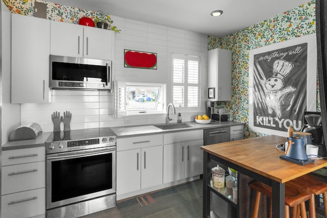kitchen with appliances with stainless steel finishes, a sink, white cabinets, decorative backsplash, and wallpapered walls