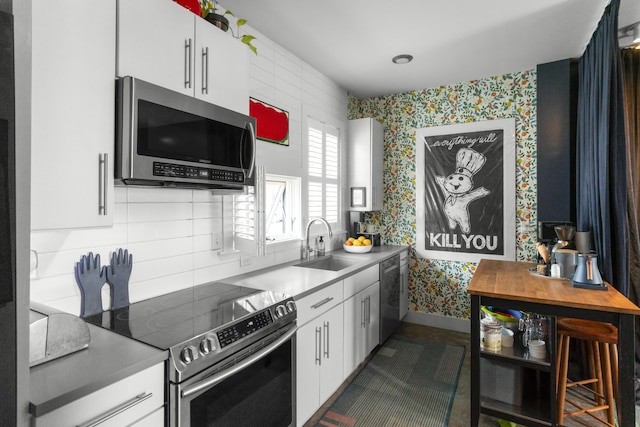 kitchen with stainless steel appliances, wallpapered walls, a sink, white cabinetry, and backsplash