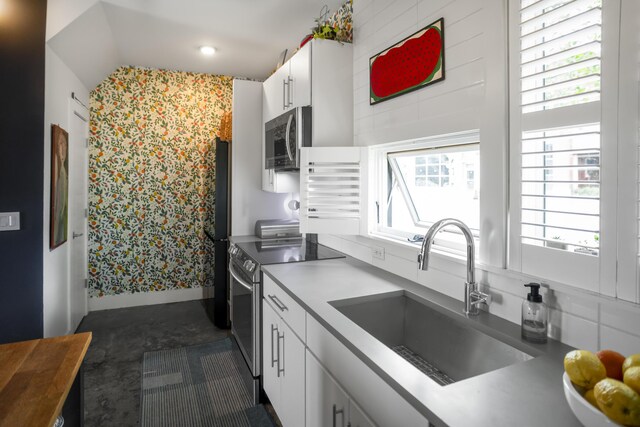 kitchen with appliances with stainless steel finishes, a sink, white cabinetry, baseboards, and wallpapered walls