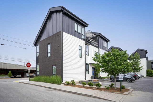 view of side of property with uncovered parking, a balcony, brick siding, and board and batten siding