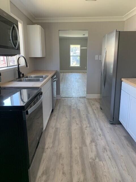 3113 10th Ave, Chattanooga, TN 37407 - kitchen featuring appliances with stainless steel finishes, healthy amount of natural light, white cabinets, ornamental molding, and light wood-style flooring