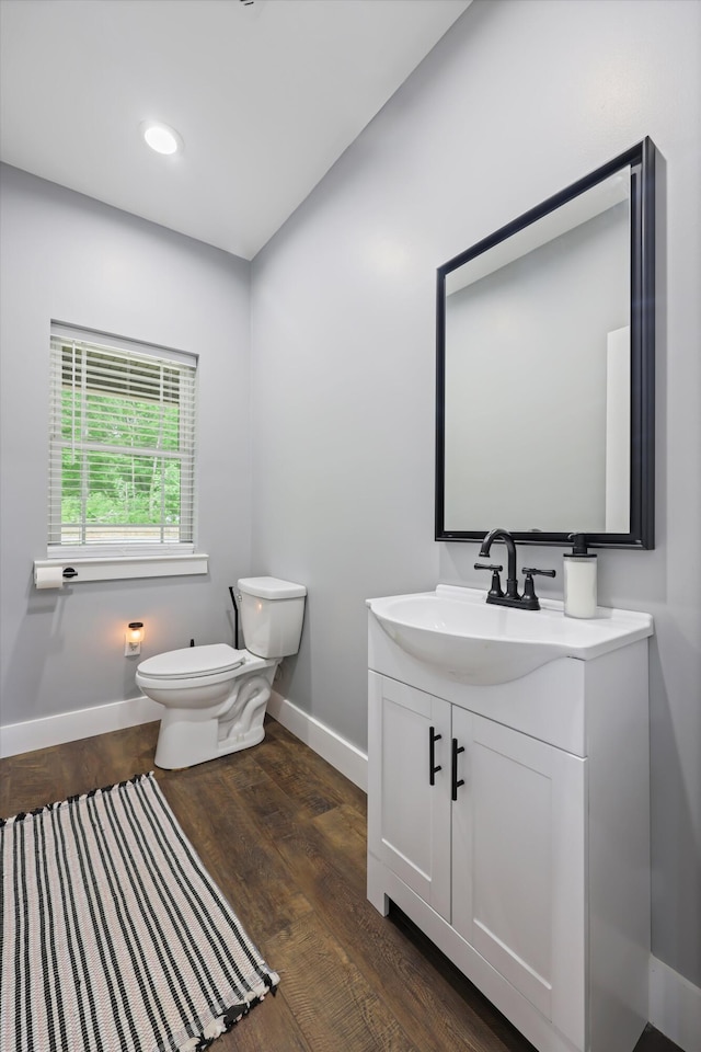 bathroom with toilet, baseboards, vanity, wood finished floors, and recessed lighting