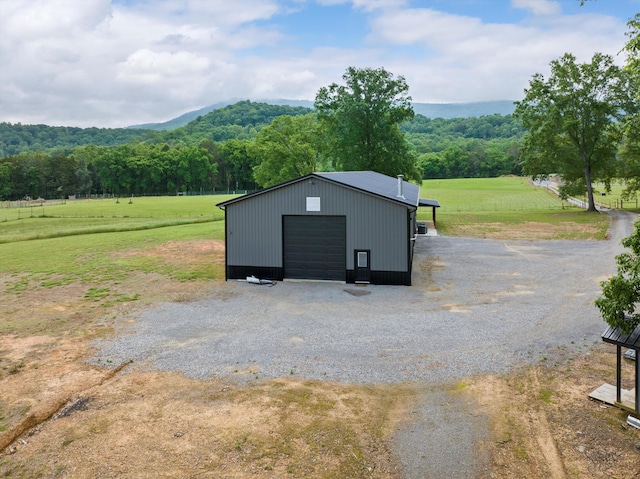 view of outbuilding with driveway, a wooded view, an outdoor structure, and a view of countryside
