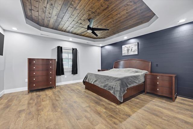 bedroom featuring a tray ceiling, wooden ceiling, baseboards, wood finished floors, and a ceiling fan
